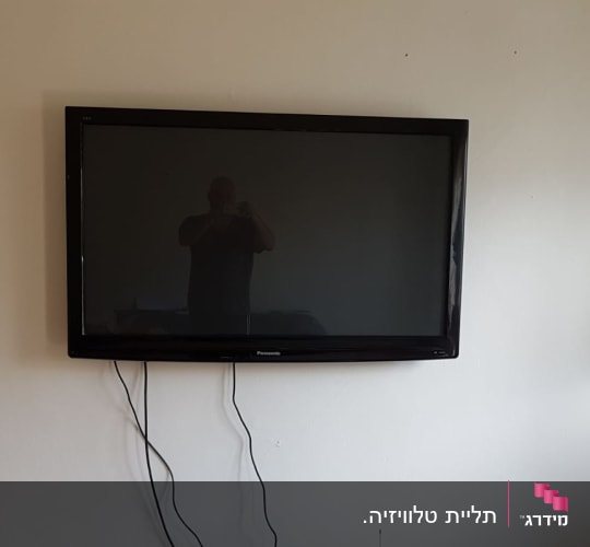 טלוויזיה תלויה על קיר עם כבלים חשמליים גלויים